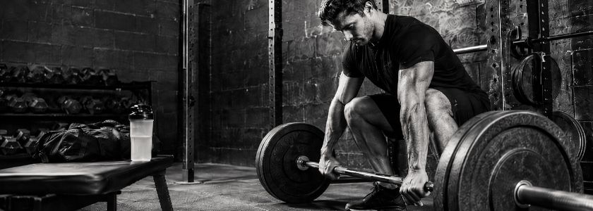 Athlete beside a loaded barbell and unbranded shaker in a high-contrast monochrome gym